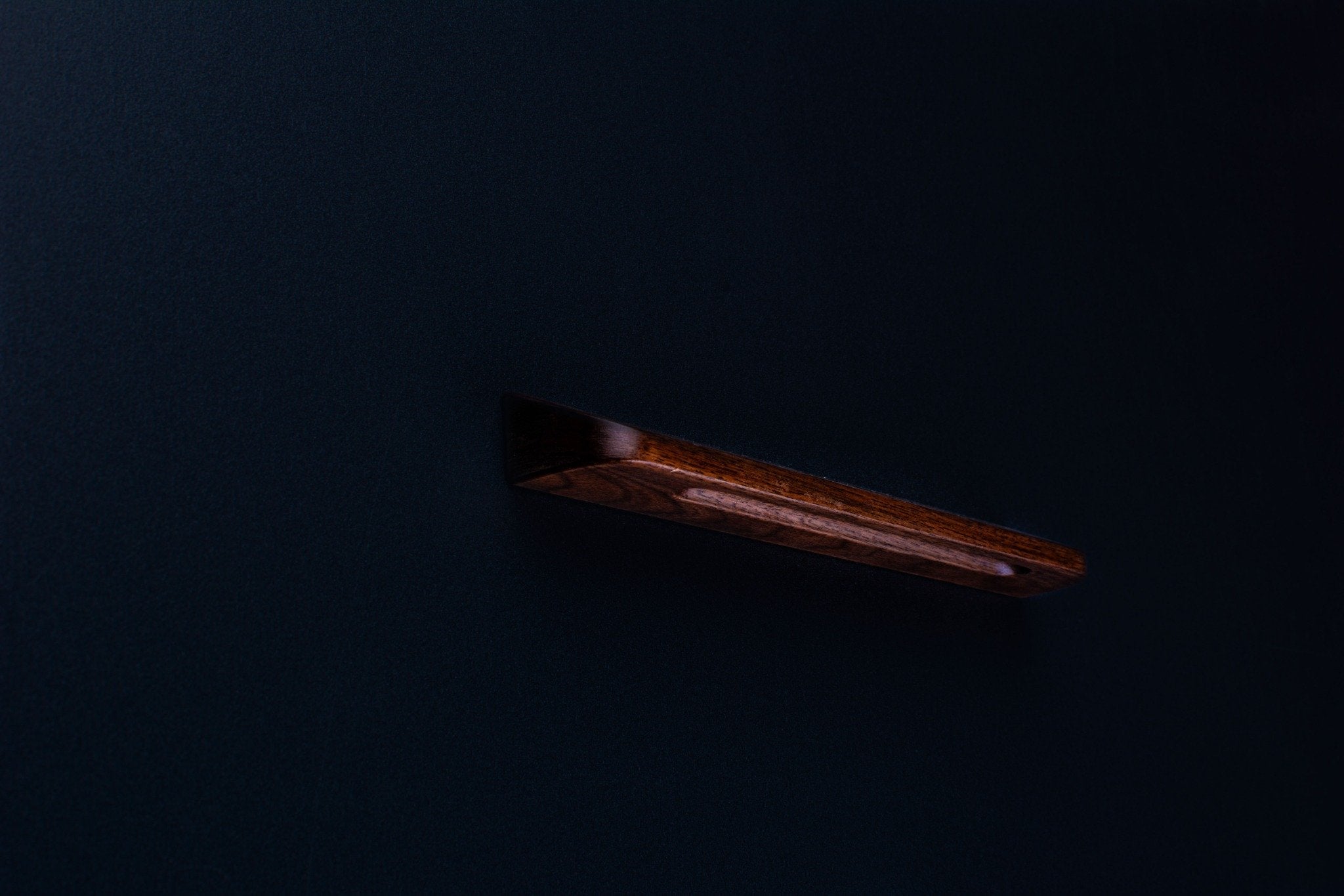 Angled side view of a dark American walnut furniture handle mounted on a black surface
