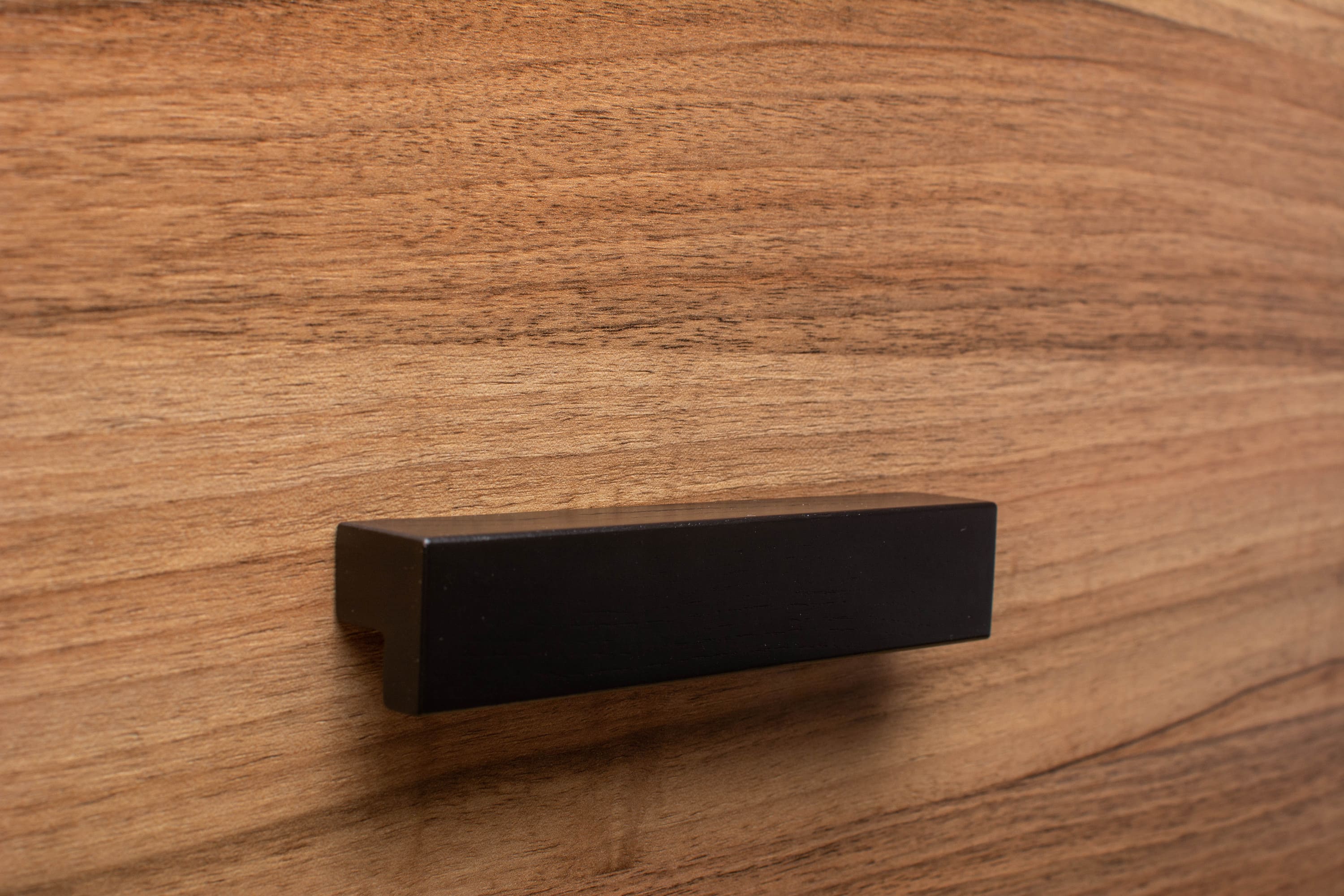 Angled view of L-form black handle mounted on walnut cabinet, creating a bold contrast.