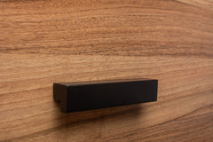 Angled view of L-form black handle mounted on walnut cabinet, creating a bold contrast.