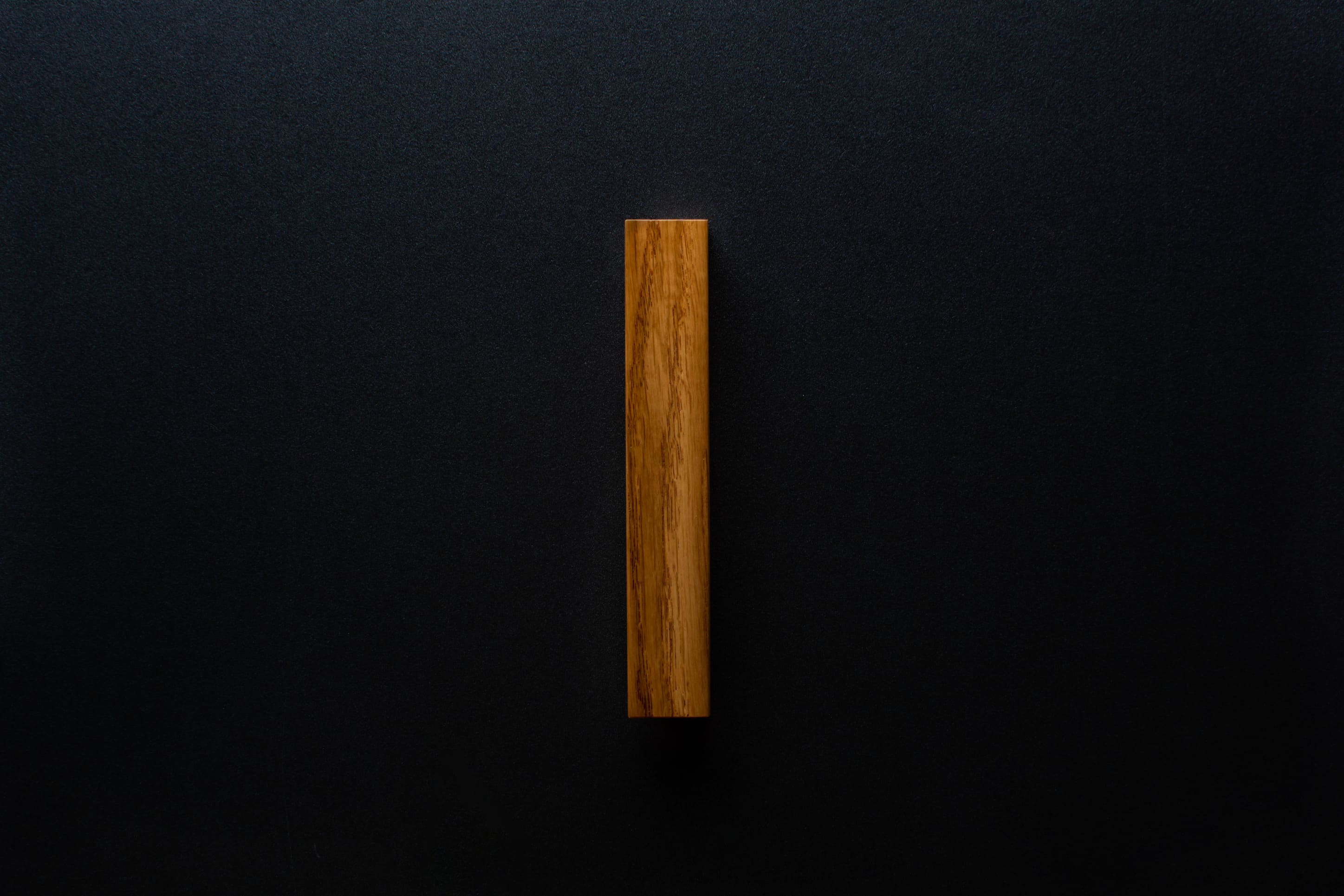 Angled view of the Modern Oak Cabinet Handle mounted on a black cabinet, capturing the natural oak texture.
