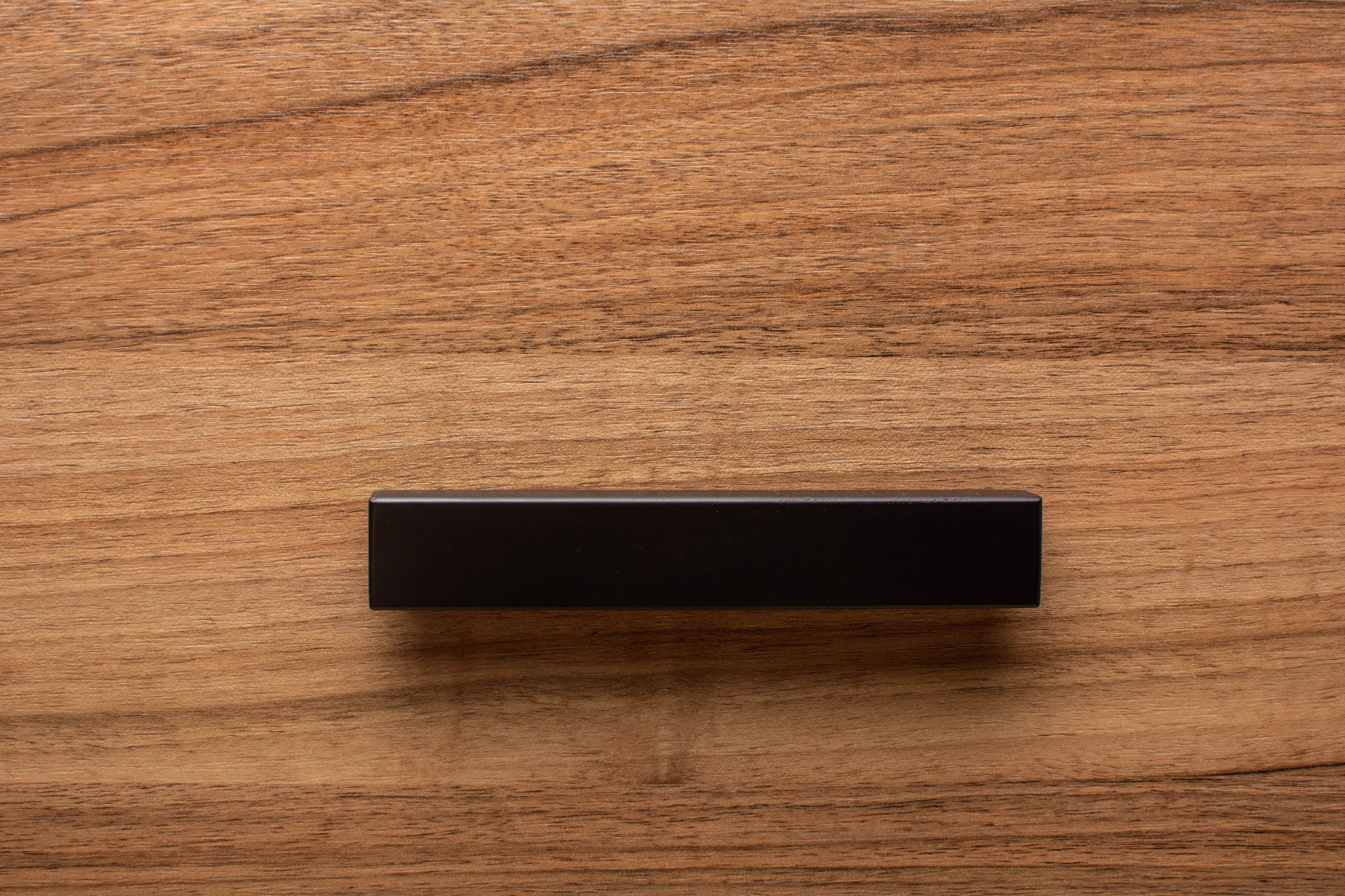 Black L-shaped wooden handle on walnut drawer, adding sleek functionality to furniture.
