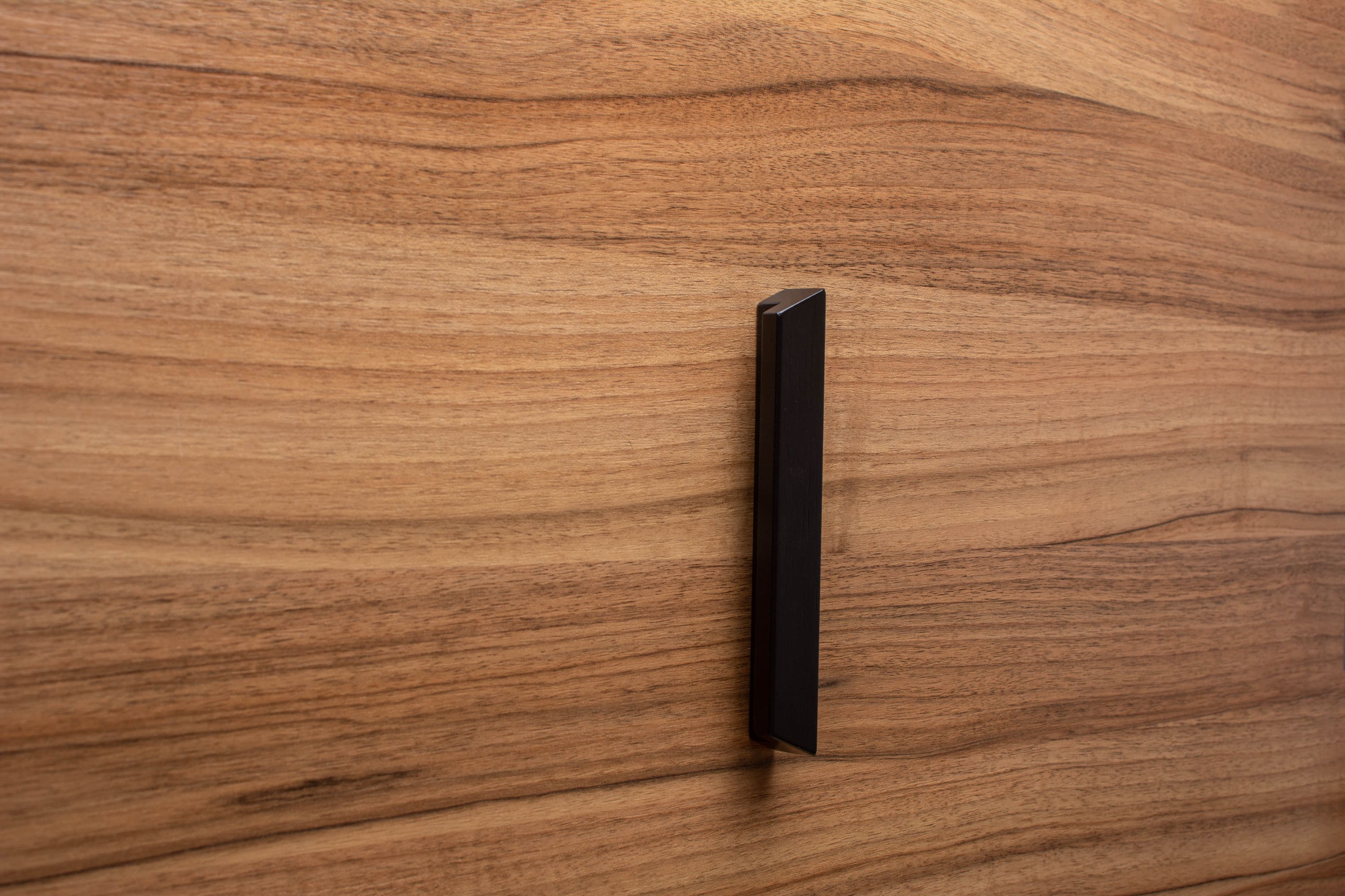 Black modern handle installed on a walnut cabinet door, creating a striking contrast between dark and light tones.