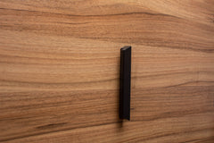 Black modern handle installed on a walnut cabinet door, creating a striking contrast between dark and light tones.