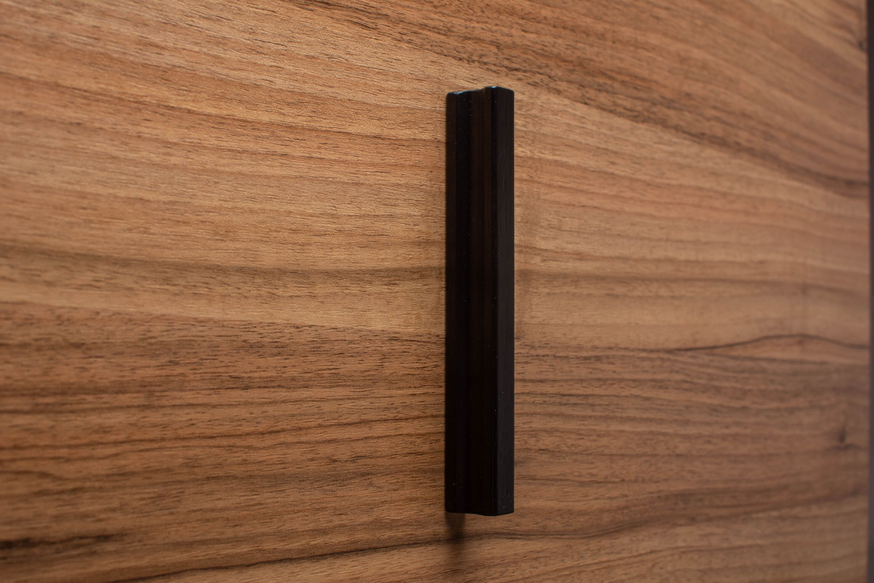 Angled photo of black wooden handle on rich walnut cabinet, emphasizing the clean lines and contrast.