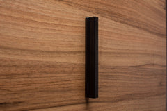 Angled photo of black wooden handle on rich walnut cabinet, emphasizing the clean lines and contrast.