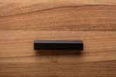 Black painted wooden cabinet handle on walnut door, blending modern design with rich wood grain.
