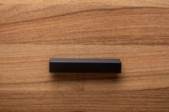 Black painted wooden cabinet handle on walnut door, blending modern design with rich wood grain.