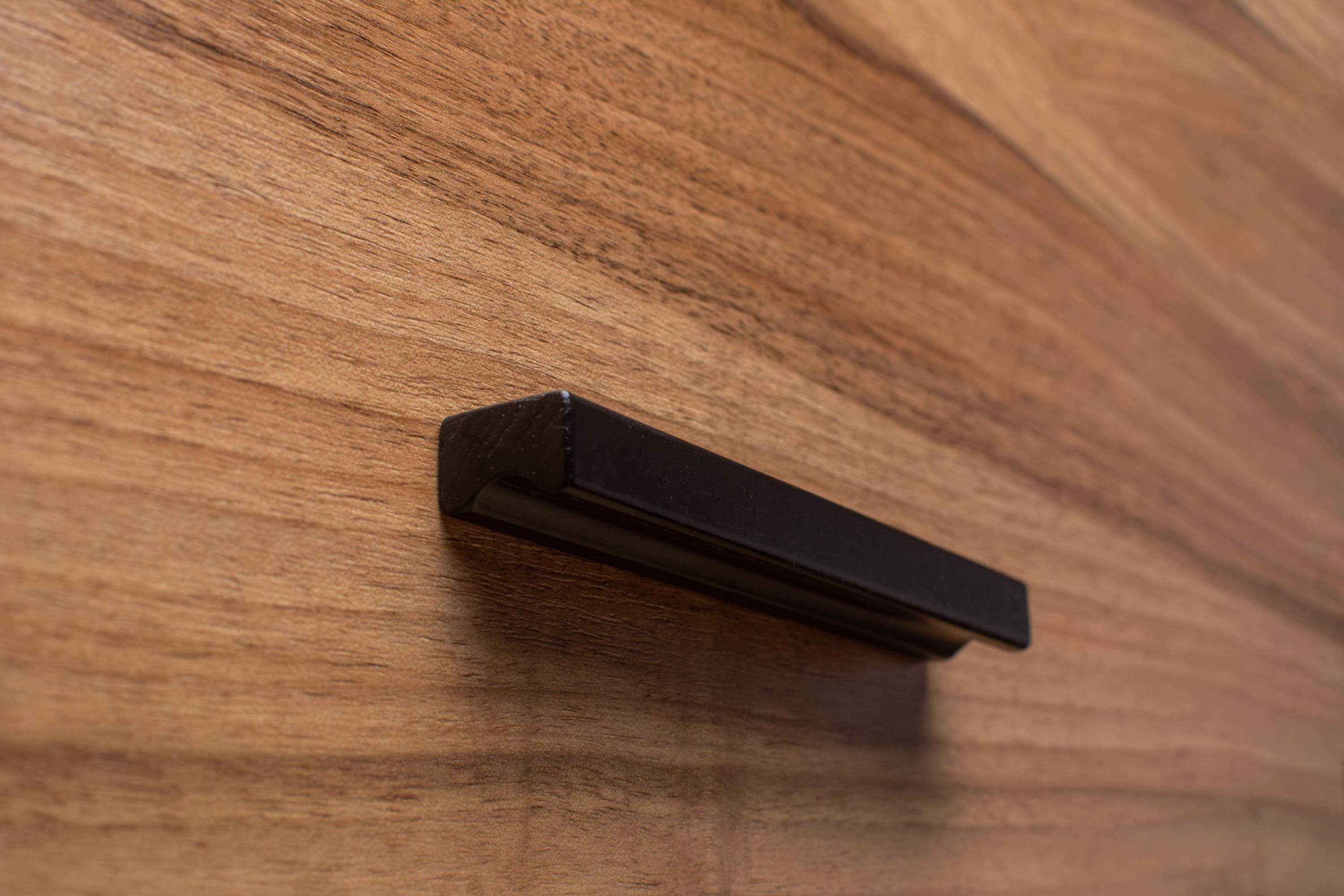 Black painted wooden cabinet handle mounted on walnut cabinet, highlighting sleek contrast in modern design.