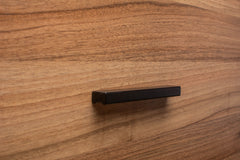 Close-up of black painted handle on walnut cabinet drawer, showing texture and craftsmanship.