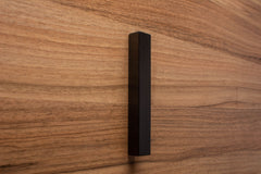 Trapezoidal black cabinet handle on walnut surface, highlighting bold angles and modern craftsmanship.