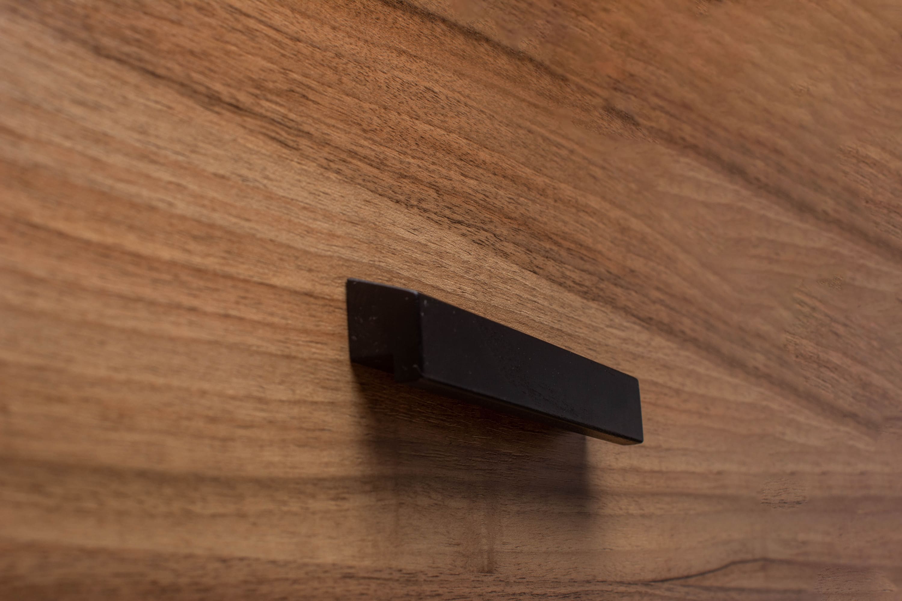 Classic black cabinet handle on walnut drawer, offering timeless elegance and sturdy design.