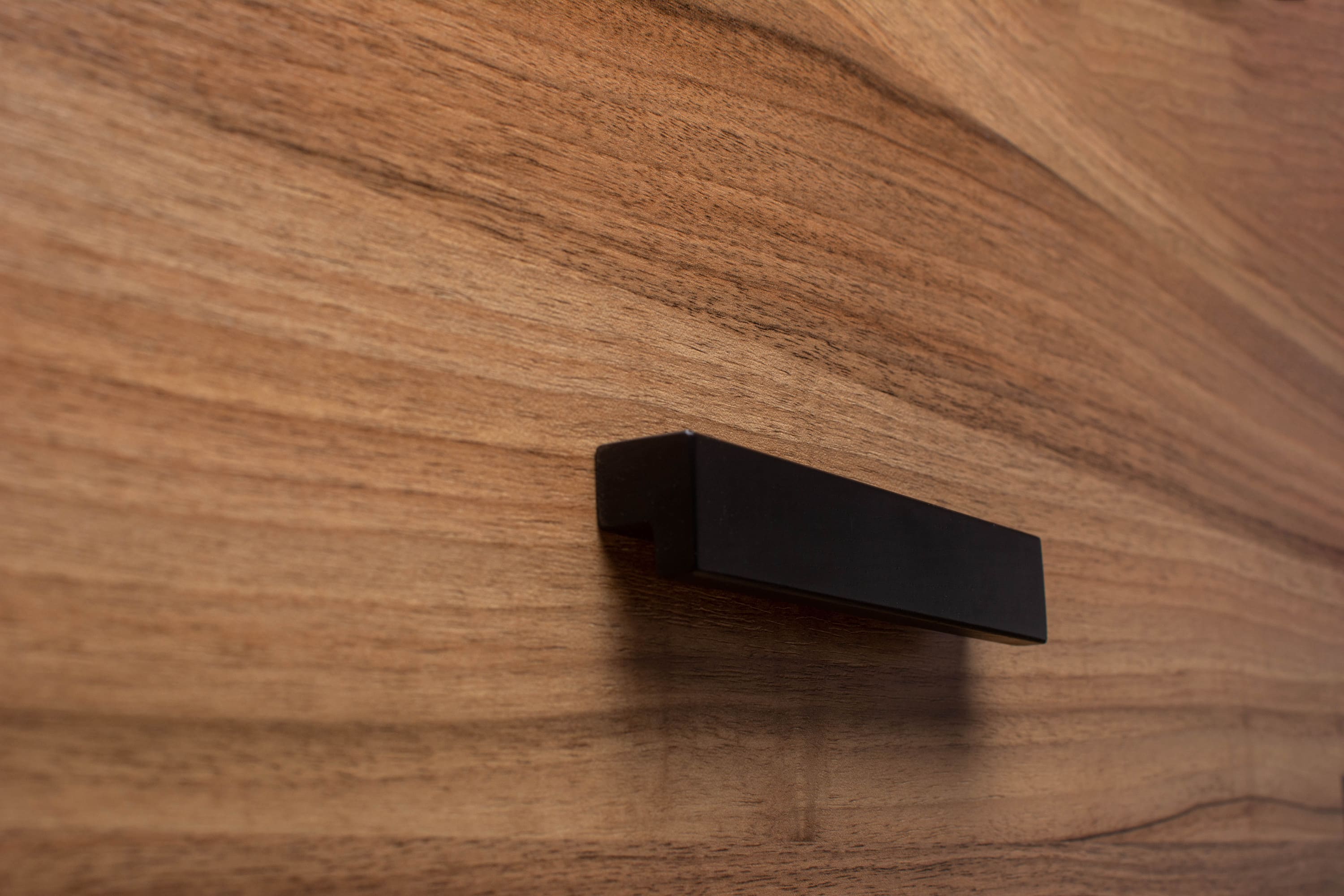 Classic black L-form handle on walnut cabinet, showcasing a bold and modern design.