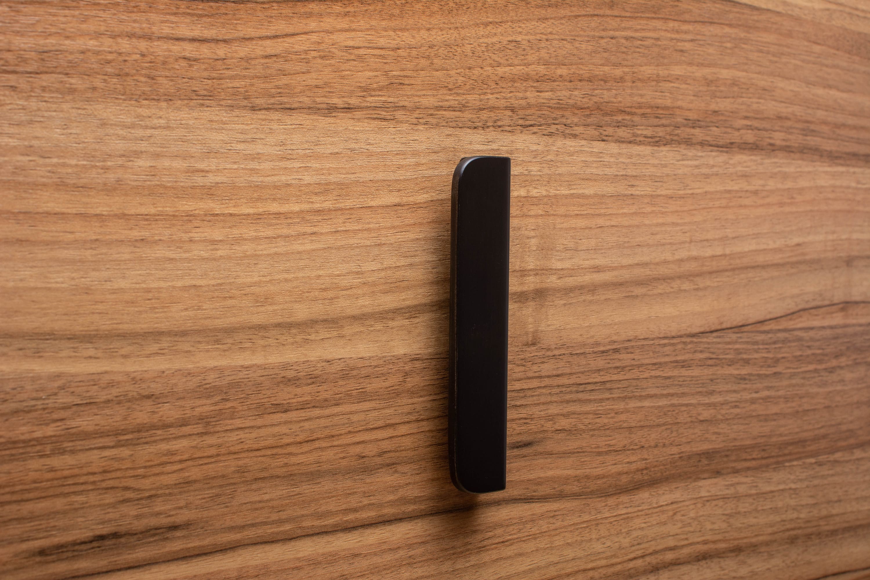 Contemporary rounded black handle with wide grip on walnut cabinet, designed for comfort and style.