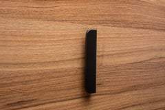 Contemporary rounded black handle with wide grip on walnut cabinet, designed for comfort and style.