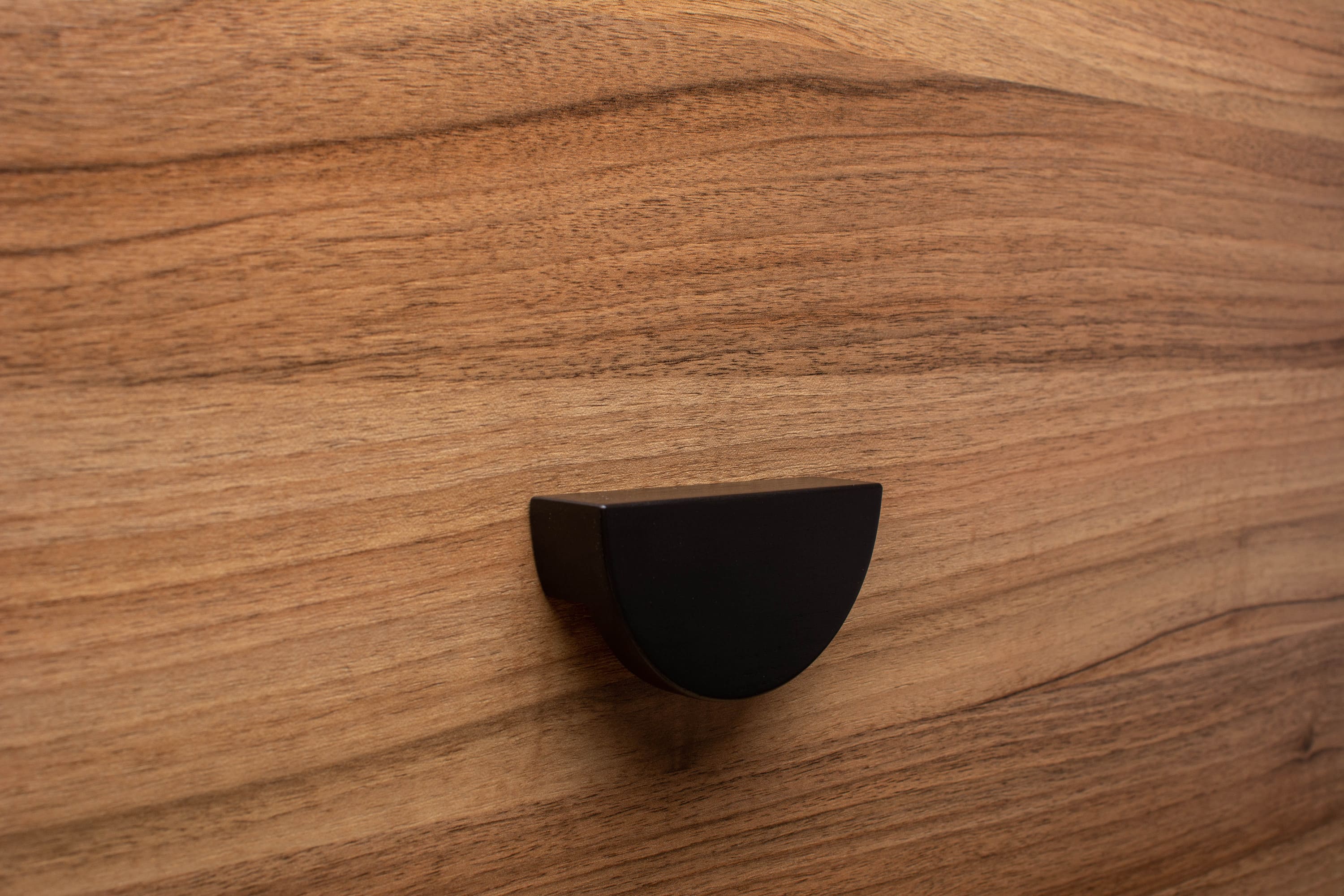 Half moon black cabinet handle on walnut furniture, adding elegance to modern decor.