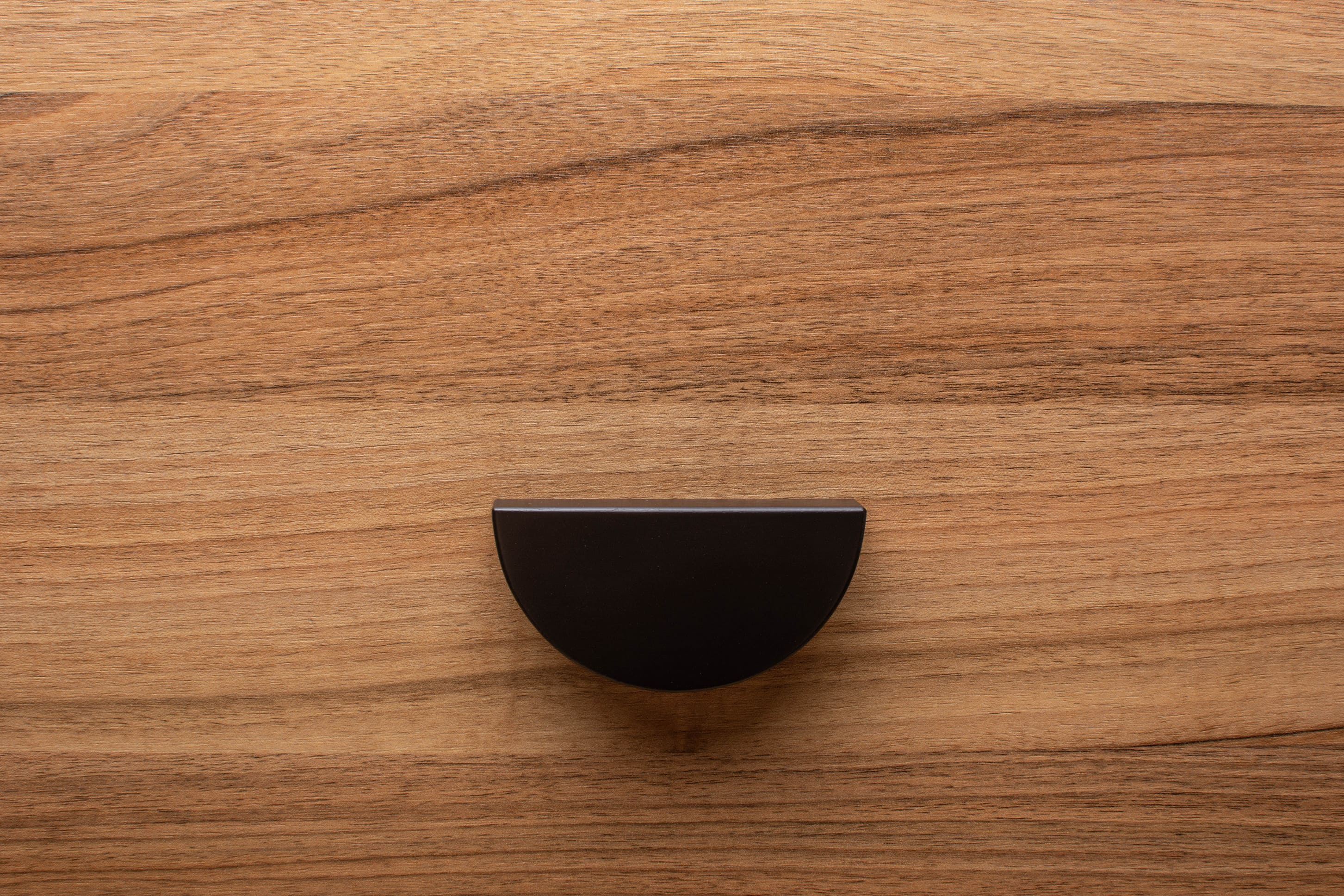 Minimalist half moon black cabinet handle on walnut drawer, perfect for modern interiors.