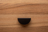 Minimalist half moon black cabinet handle on walnut drawer, perfect for modern interiors.