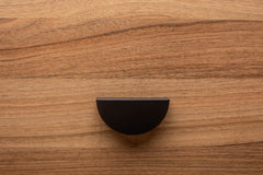 Minimalist half moon black cabinet handle on walnut drawer, perfect for modern interiors.