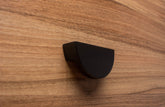 Half moon black wooden handle on walnut cabinet, creating a sleek modern look.