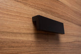 L-form black cabinet handle with wide grip on walnut drawer, ideal for modern furniture.