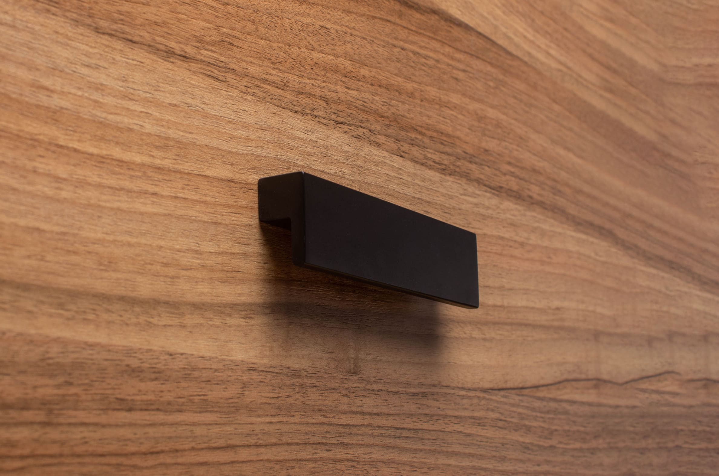 L-form black cabinet handle with wide grip on walnut drawer, ideal for modern furniture.