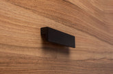 L-form black cabinet handle with wide grip on walnut drawer, ideal for modern furniture.