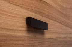 L-form black cabinet handle with wide grip on walnut drawer, ideal for modern furniture.