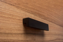 L-form black handle on walnut cabinet, blending contemporary design with rich wood texture.
