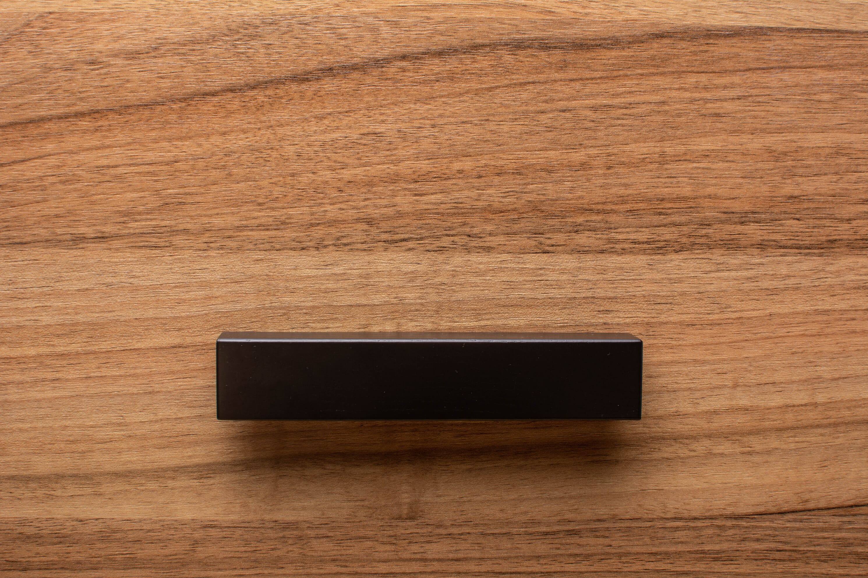Close-up of L-shaped black wooden handle on walnut drawer, highlighting sleek angles and craftsmanship.