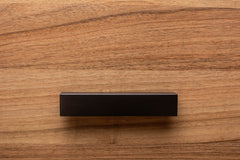 Close-up of L-shaped black wooden handle on walnut drawer, highlighting sleek angles and craftsmanship.