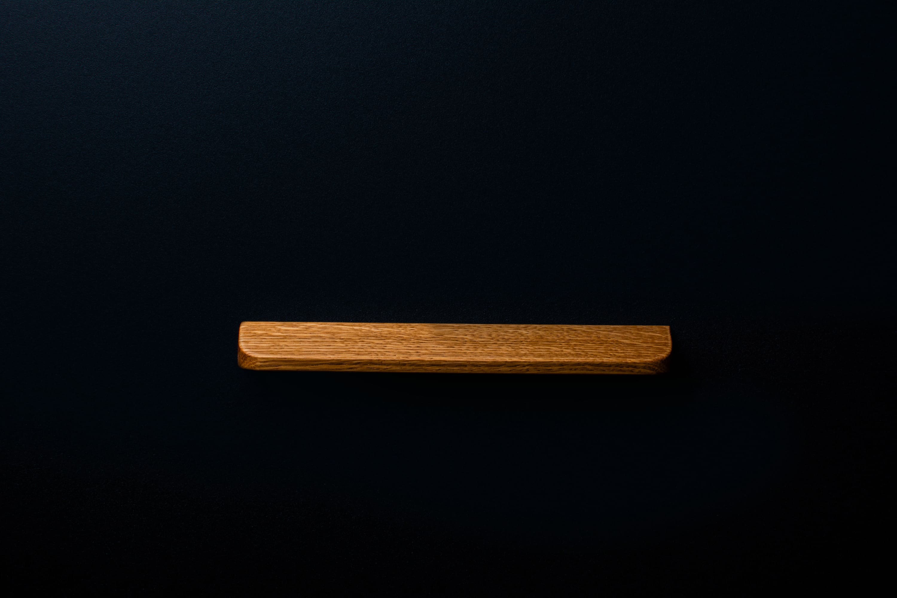 Long solid oak handle with matte coating on black wooden furniture