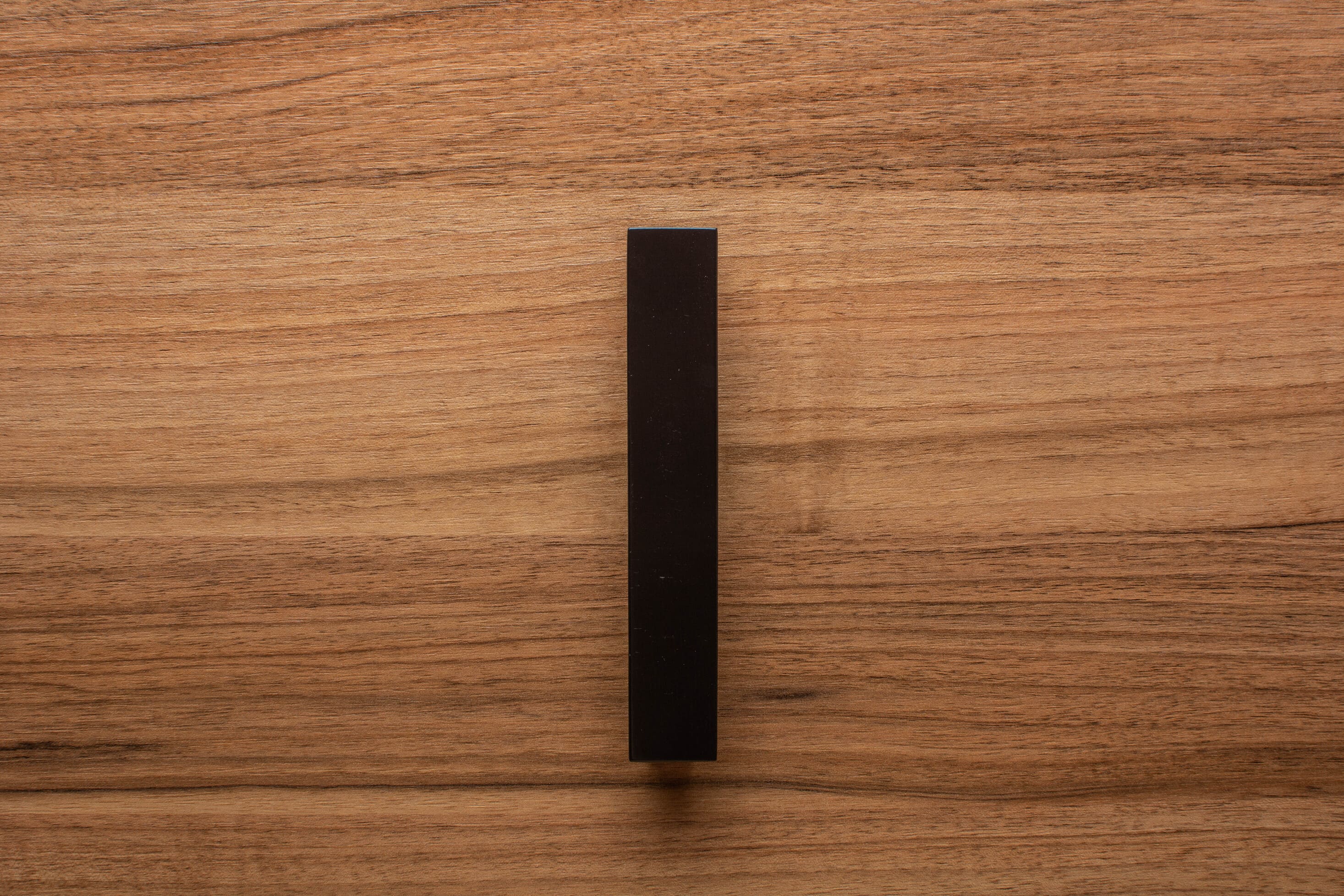Matte black trapezoidal handle mounted on walnut cabinet, perfect for minimalist interior decor.