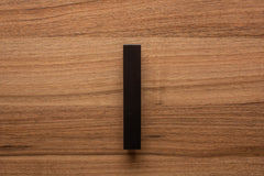 Matte black trapezoidal handle mounted on walnut cabinet, perfect for minimalist interior decor.