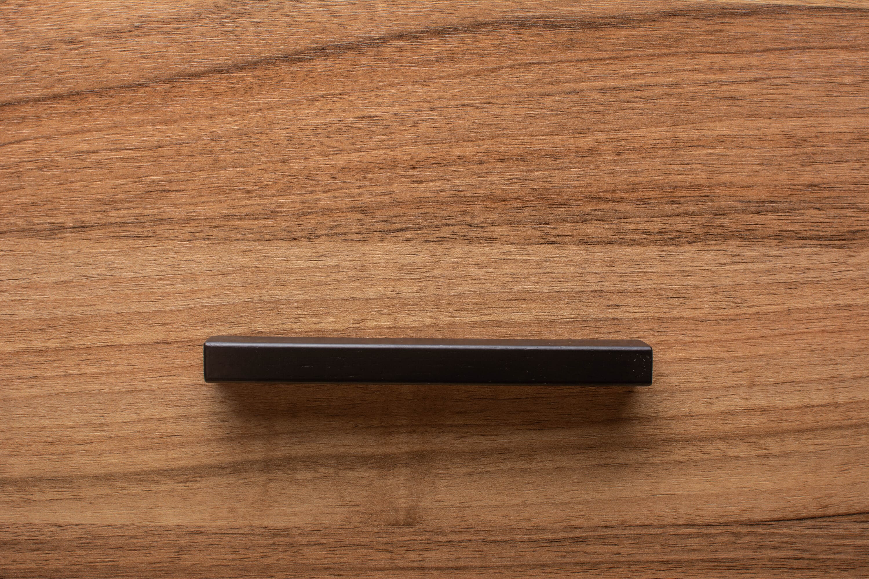 Side view of black cabinet handle installed on walnut wood, showcasing the handle's minimalist design.