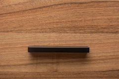 Side view of black cabinet handle installed on walnut wood, showcasing the handle's minimalist design.
