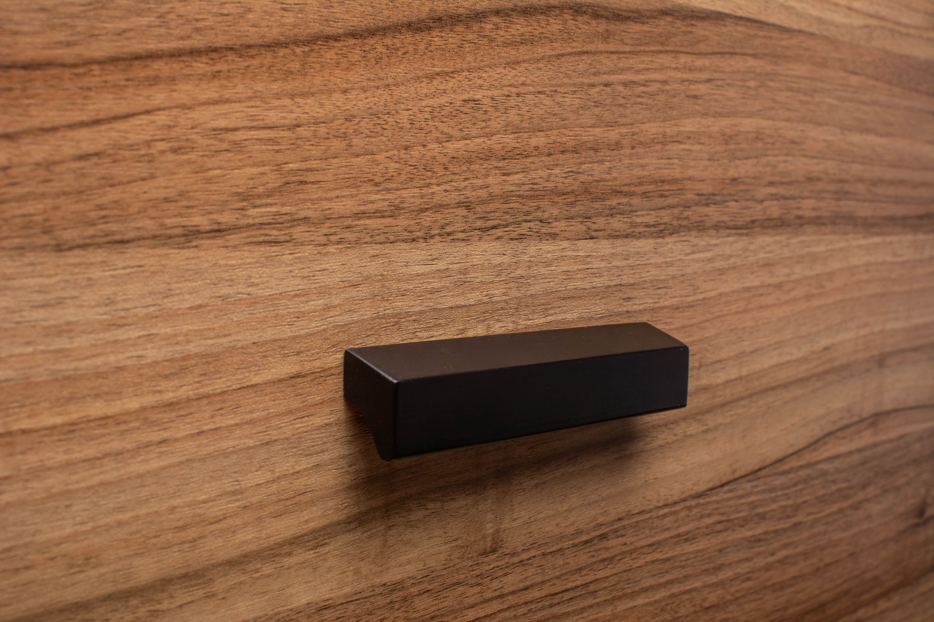 Black cabinet handle on walnut wood, highlighting minimalist style and natural tones.