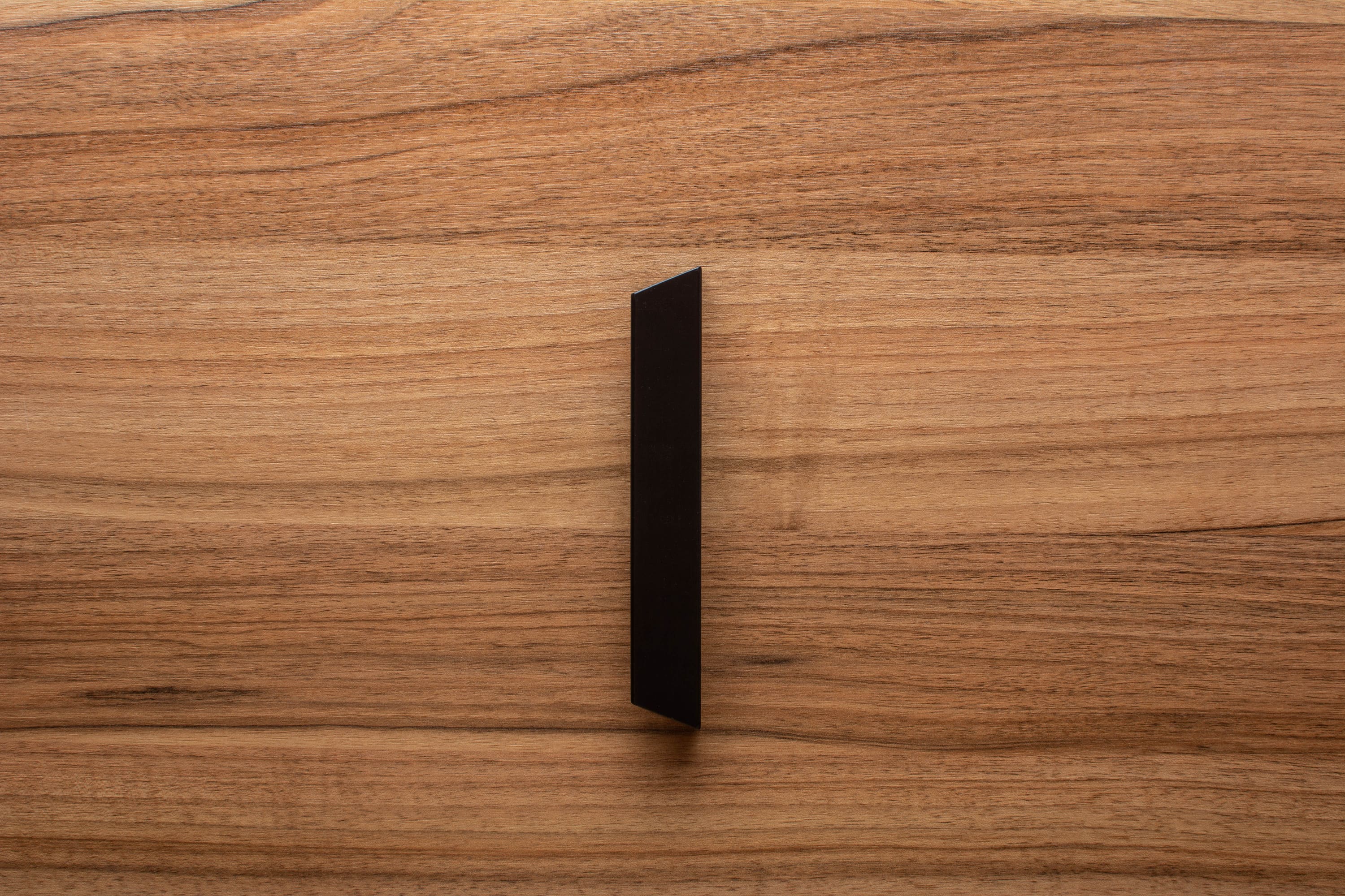 Minimalist black handle on walnut cabinet, perfect for modern kitchen or living spaces.
