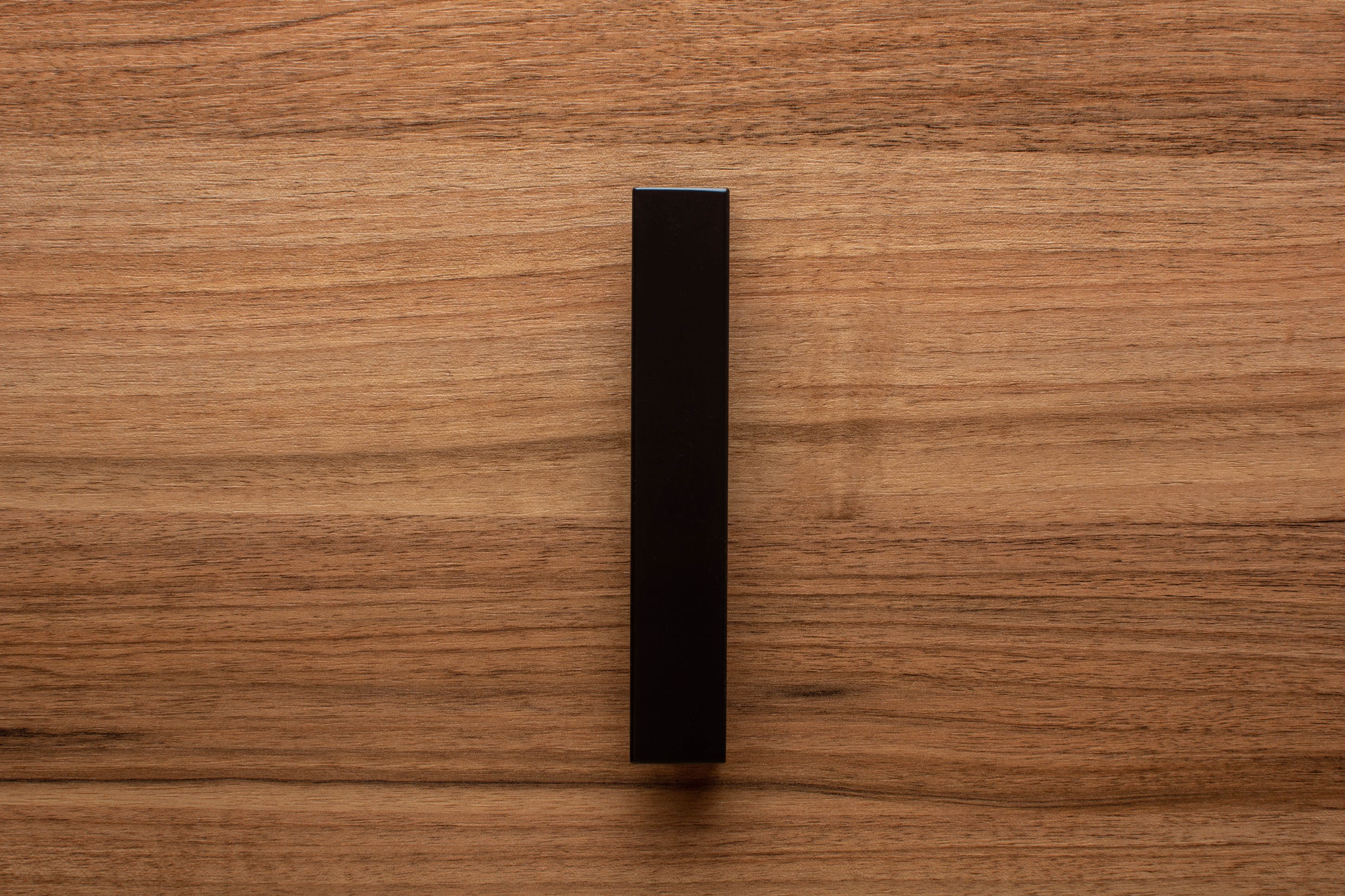 L-shaped black cabinet handle on walnut drawer, a minimalist touch for modern furniture.
