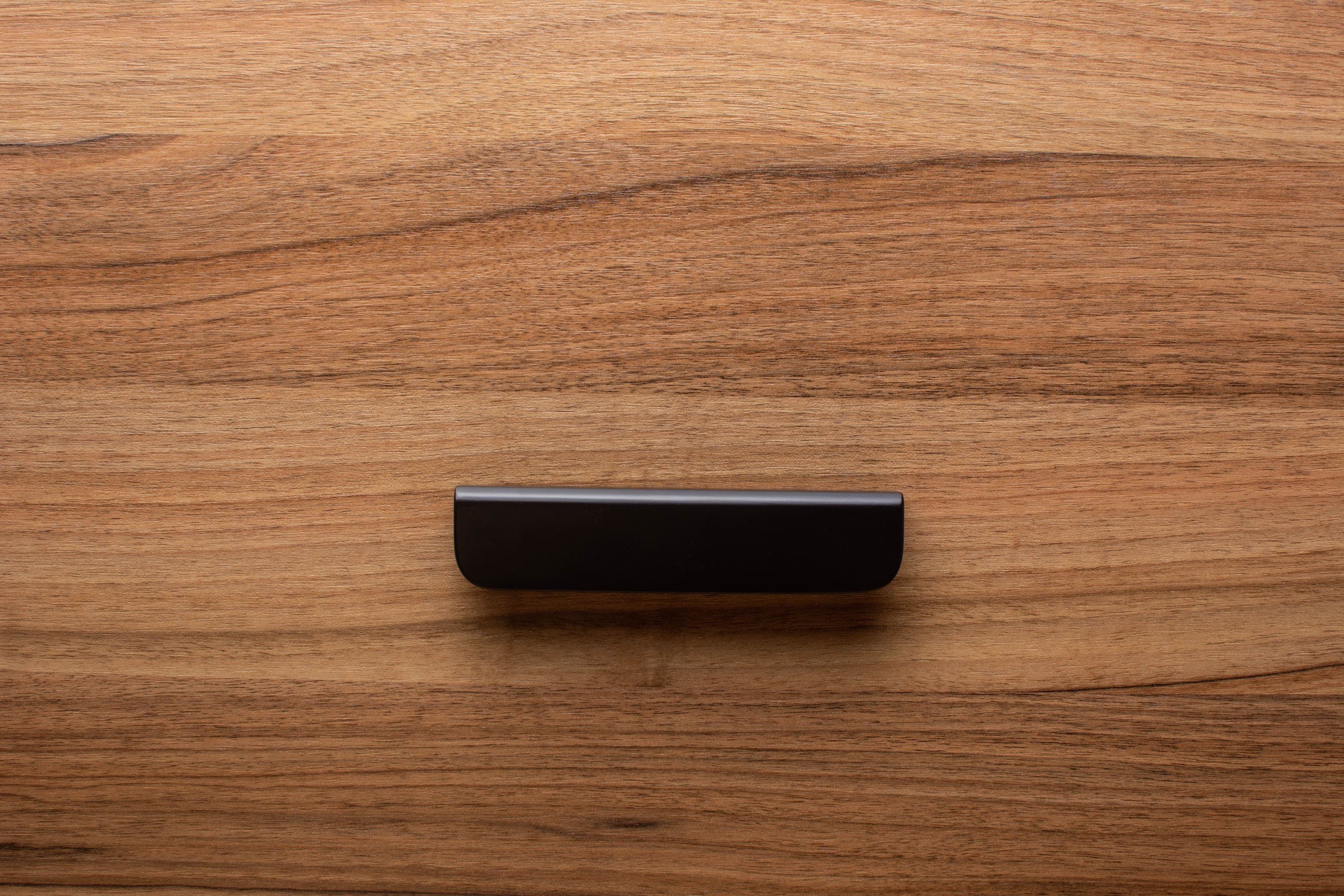 Smooth rounded black handle with wide grip on walnut cabinet, adding a minimalist touch.