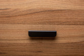 Smooth rounded black handle with wide grip on walnut cabinet, adding a minimalist touch.