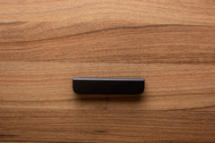 Smooth rounded black handle with wide grip on walnut cabinet, adding a minimalist touch.