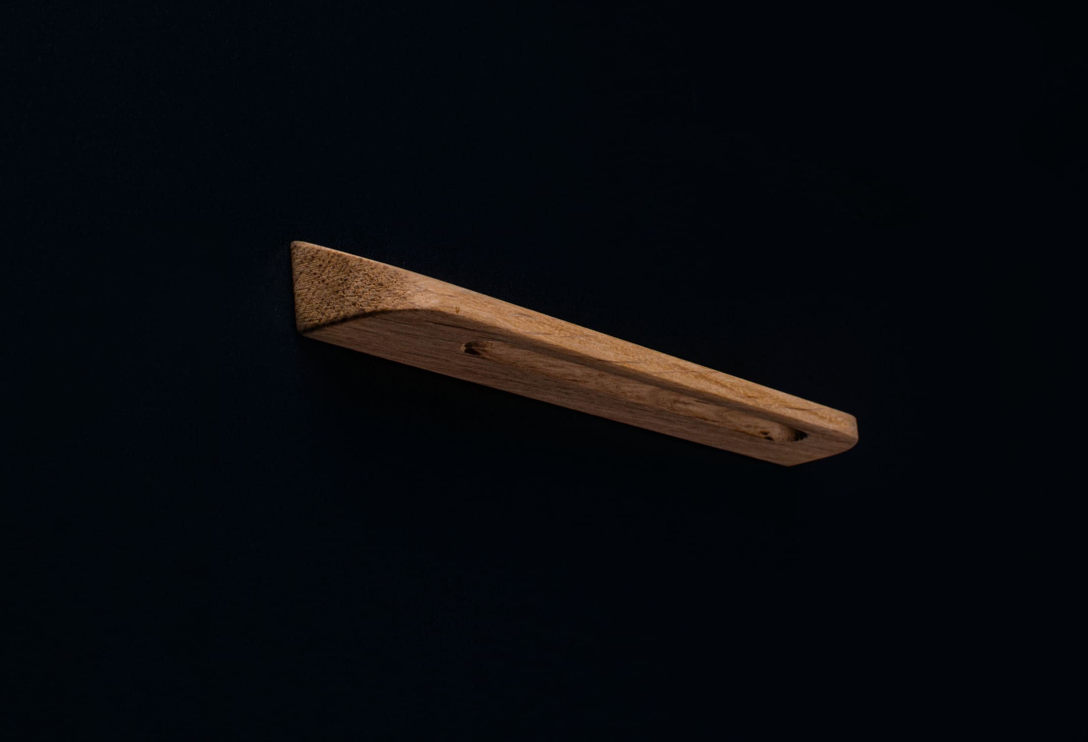 Hand-sanded oak handle with no finish, side view on a black cabinet door
