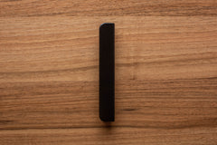 Minimal rounded black handle on walnut cabinet drawer, combining function and style.