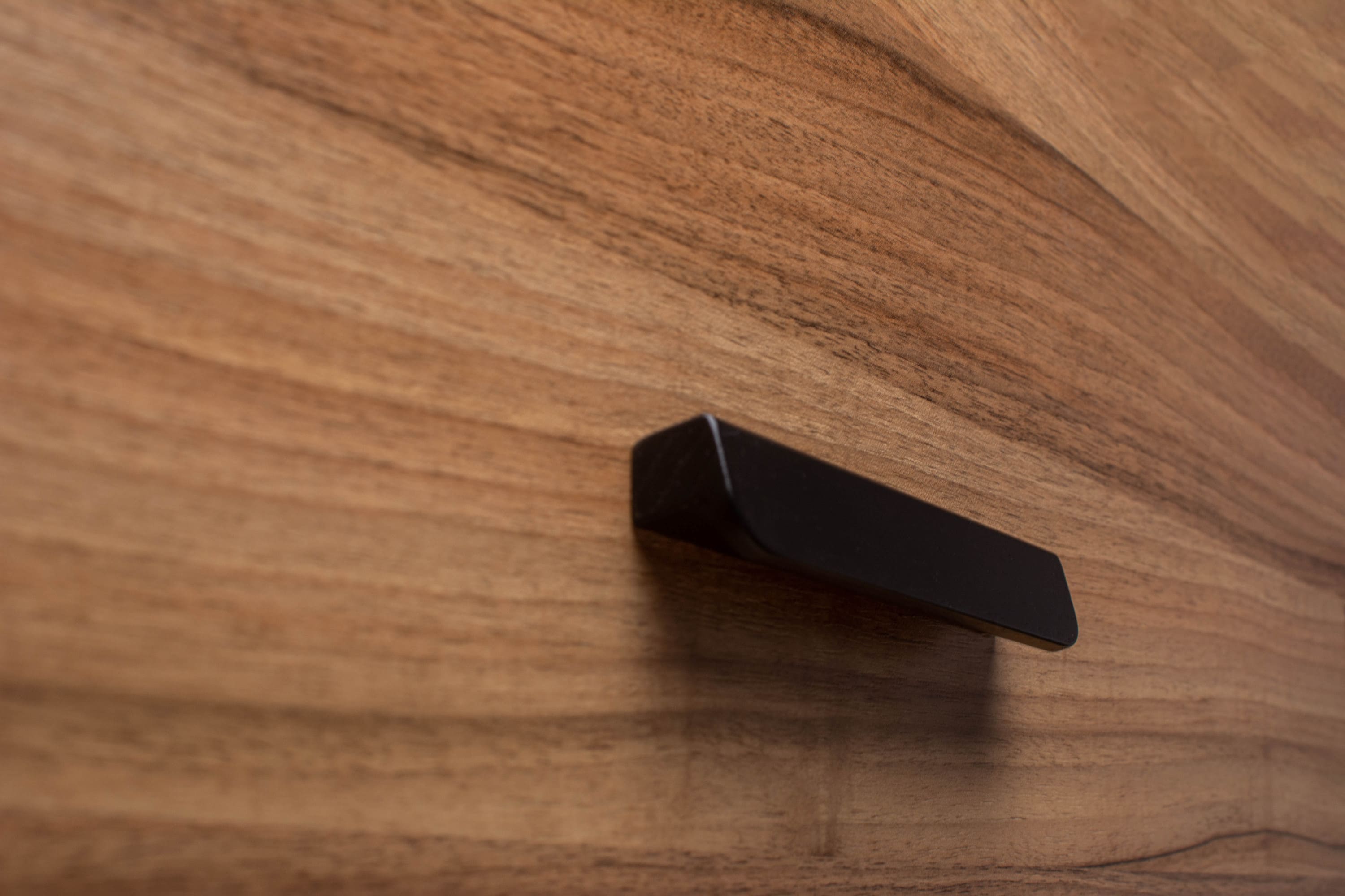 Minimalistic rounded black handle on walnut cabinet, offering sleek and subtle elegance.
