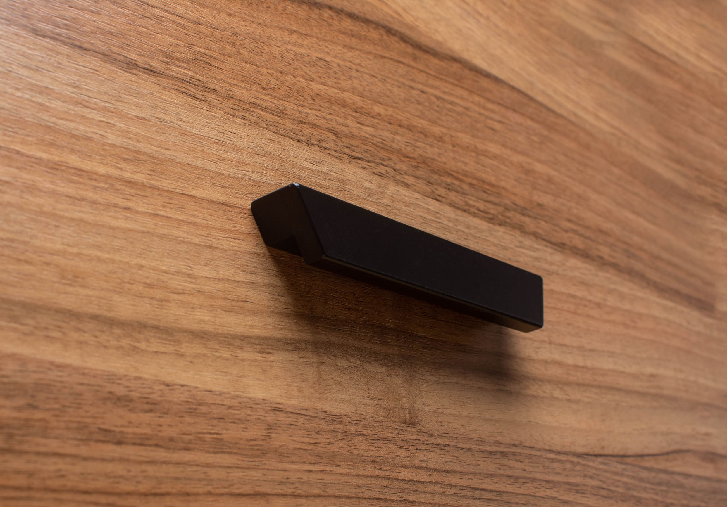 Modern black handle on walnut cabinet, showcasing sleek minimalist design and bold contrast.