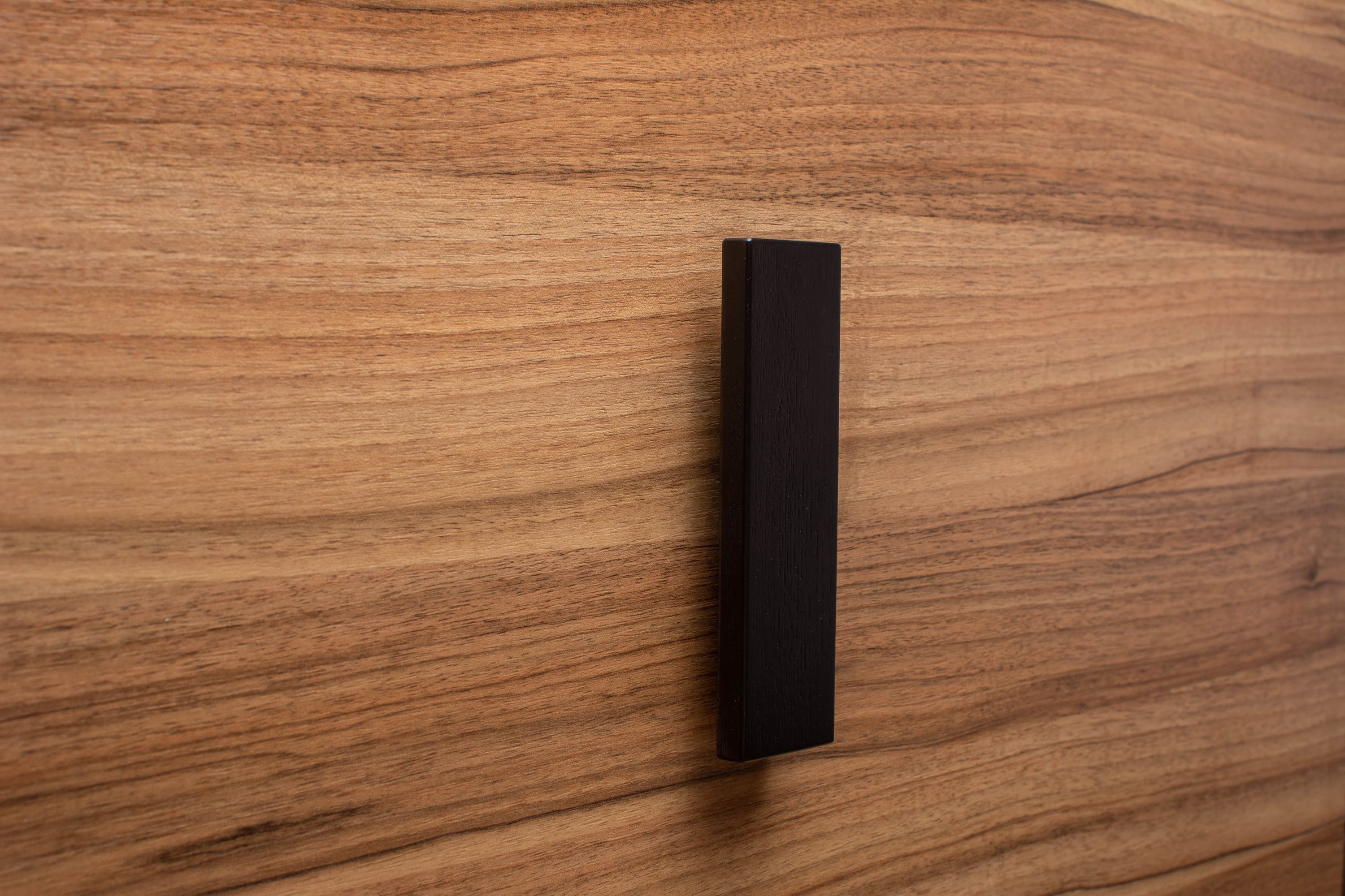 Modern black L-form handle with wide grip on walnut drawer, offering both elegance and practicality.