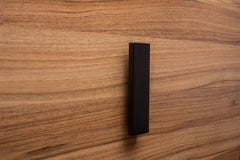 Modern black L-form handle with wide grip on walnut drawer, offering both elegance and practicality.