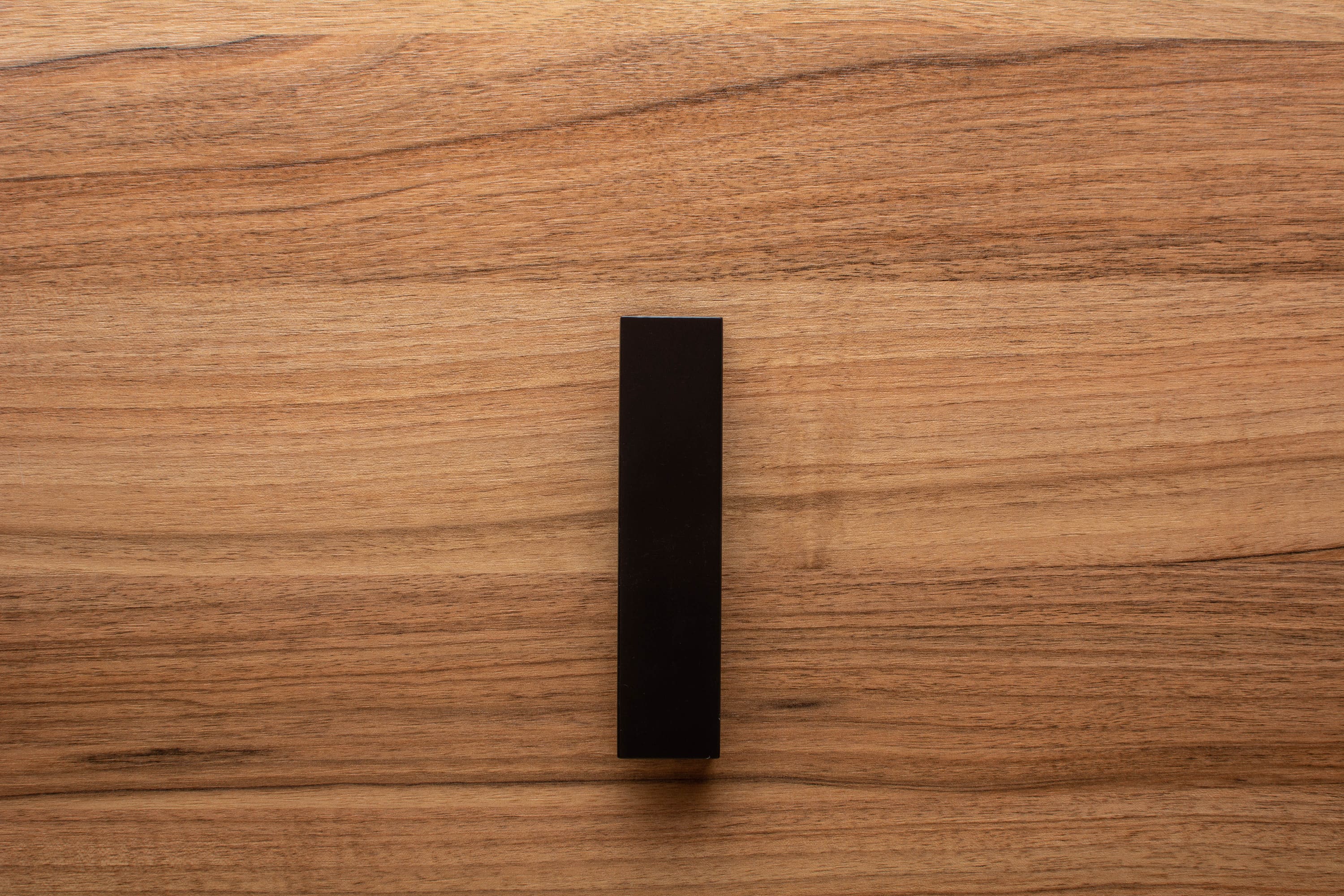 Modern black L-form handle with wide grip on walnut drawer, offering both elegance and practicality.
