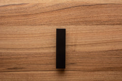 Modern black L-form handle with wide grip on walnut drawer, offering both elegance and practicality.