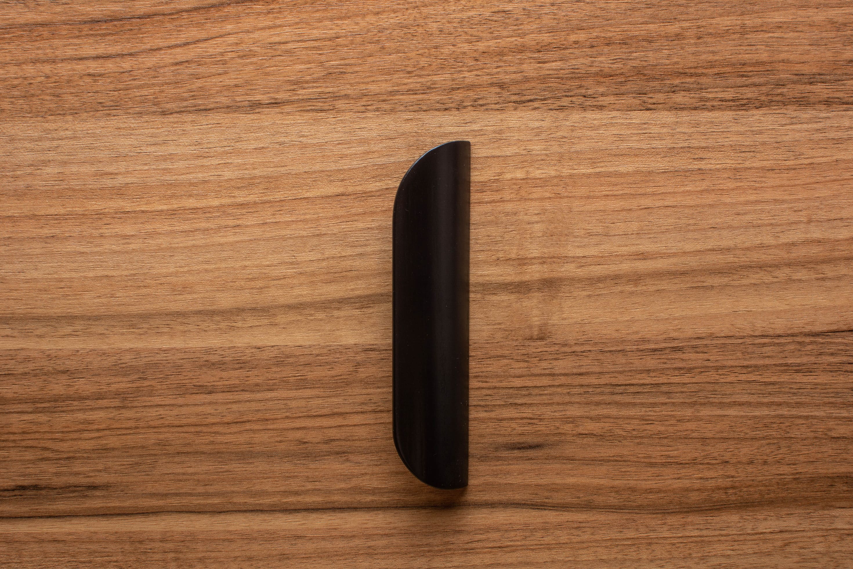 Minimalist rounded black handle on walnut cabinet, offering a modern and polished look.